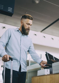 Low angle view of businessman scanning ticket on smart phone at airport check-in counter