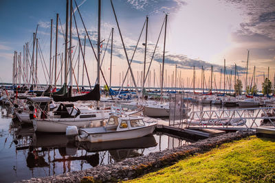 Sailboats moored in harbor at sunset