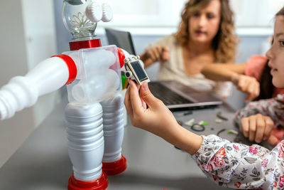 Female student holding solar panel over recycled toy robot in a robotics class