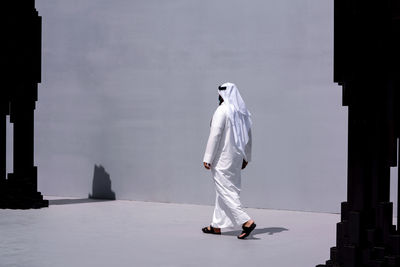Man in arabic traditional clothing walking between pillars on the grey background