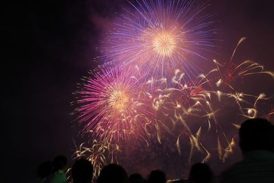 Low angle view of silhouette people looking at firework explosion at night