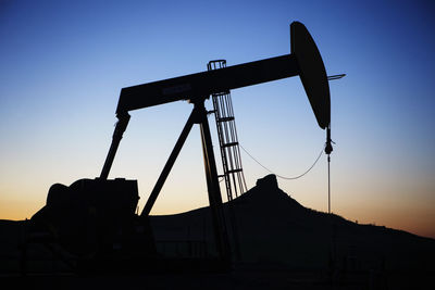 Silhouette oil pump on field against sky during sunset