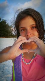 Portrait of girl making heart shape at beach