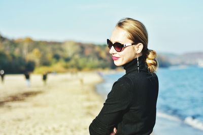 Portrait of young woman wearing sunglasses standing against sky