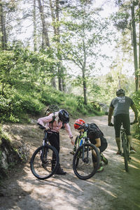 Woman assisting male friend repairing cycle while kneeling on footpath