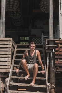 Young handsome caucasian man with a sleeve tattoo sits on the wooden stairs of a cozy cafe
