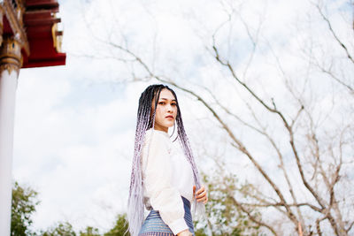 Portrait of young woman standing against trees