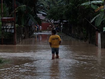 Rear view of man standing on wet road during rainy season