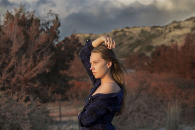 Side view of young woman standing against trees