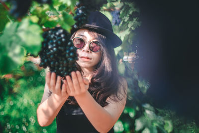 Portrait of young woman wearing sunglasses standing against plants