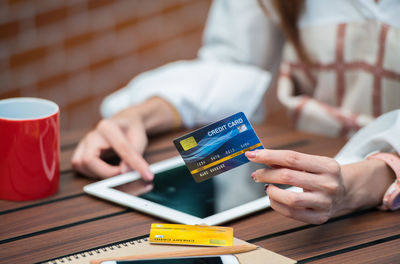 Midsection of woman using digital tablet with credit card at table in cafe