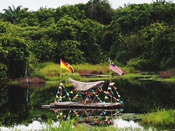 Flags and decoration on wooden raft moored at lake against trees