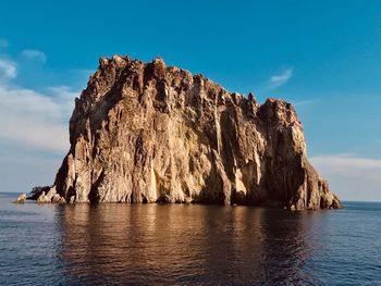 Rock formation by sea against blue sky