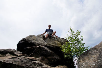 Low angle view of young man sitting on cliff against sky