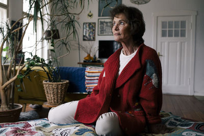 Thoughtful senior woman in sweater sitting on bed at home