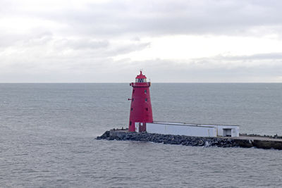 Lighthouse on sea by building against sky