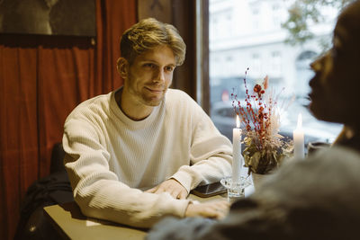 Smiling man looking at girlfriend while sitting at table during date in bar