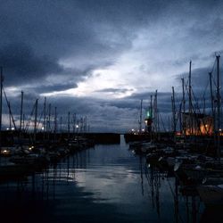 Boats in harbor against cloudy sky