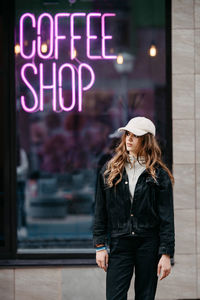 A teenage girl stands near the neon sign coffee shop. youth culture. real beautiful people. 