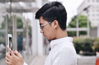 Side view of young man wearing eyeglasses using smart phone in city