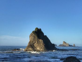 Rock on beach against clear blue sky