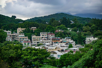 Buildings amidst trees and mountains against cloudy sky