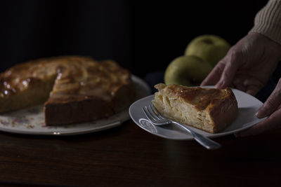 Female hands supporting a plate with a slice of apple pie. dark mood. 