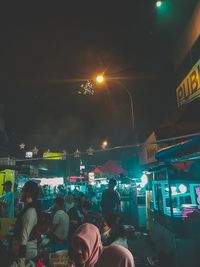 Rear view of people walking on illuminated street at night