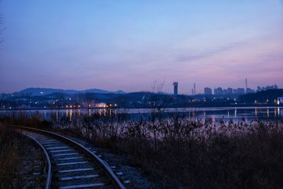 Railroad tracks by lake against sky during sunrise