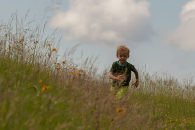 Full length of smiling boy in grass against sky