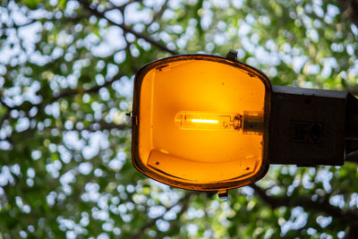 Low angle view of yellow street lamp with bokeh background of trees