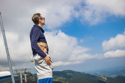 Father and son looking at view while standing against sky