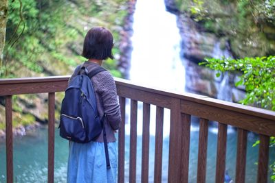 Rear view of woman looking at waterfall standing by railing