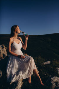 Young woman sitting on field against clear sky