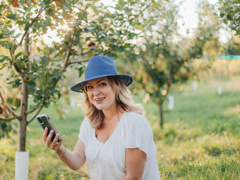 Portrait of smiling young woman holding smart phone while standing outdoors