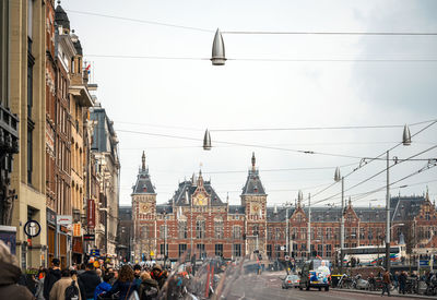 People on road against amsterdam centraal railway station and sky in city