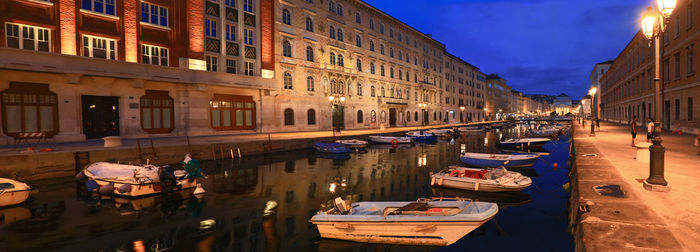 Boats moored in canal amidst buildings in city at night