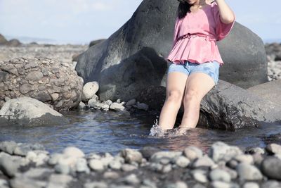 Low section of woman sitting on rock at beach