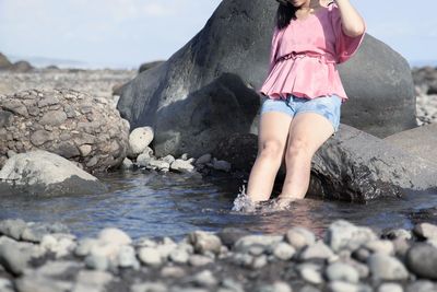 Midsection of woman sitting on rock in lake