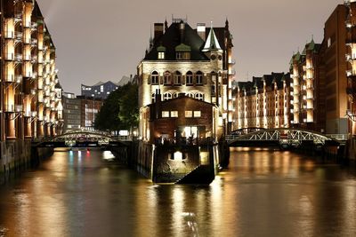 Illuminated buildings by river in city at night