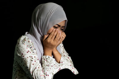 Portrait of person hiding face against black background