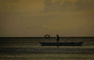 Silhouette man fishing in sea against sky during sunset