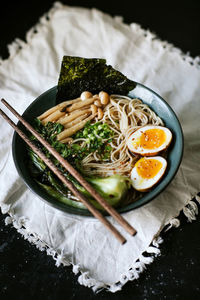 From above of ceramic bowl with delicious ramen and chopsticks placed on table covered with white tablecloth