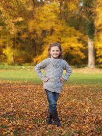 Portrait of smiling cute girl standing on field against trees at park