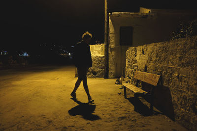 Rear view of man standing on street against building at night