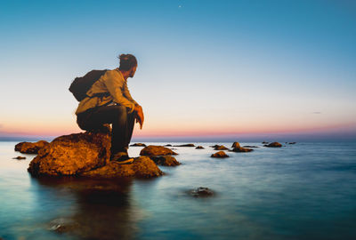 Man standing on rock in sea against clear sky