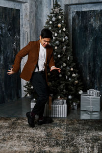 Full length of young man standing by christmas tree