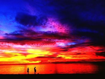 Silhouette people on beach against dramatic sky during sunset