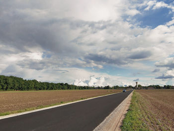 Road by agricultural field against sky
