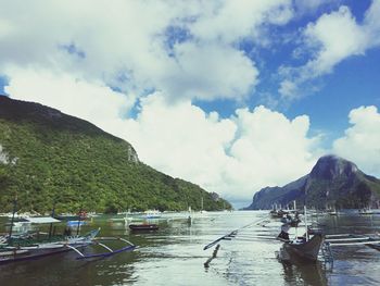 Boats moored on sea by mountains against sky